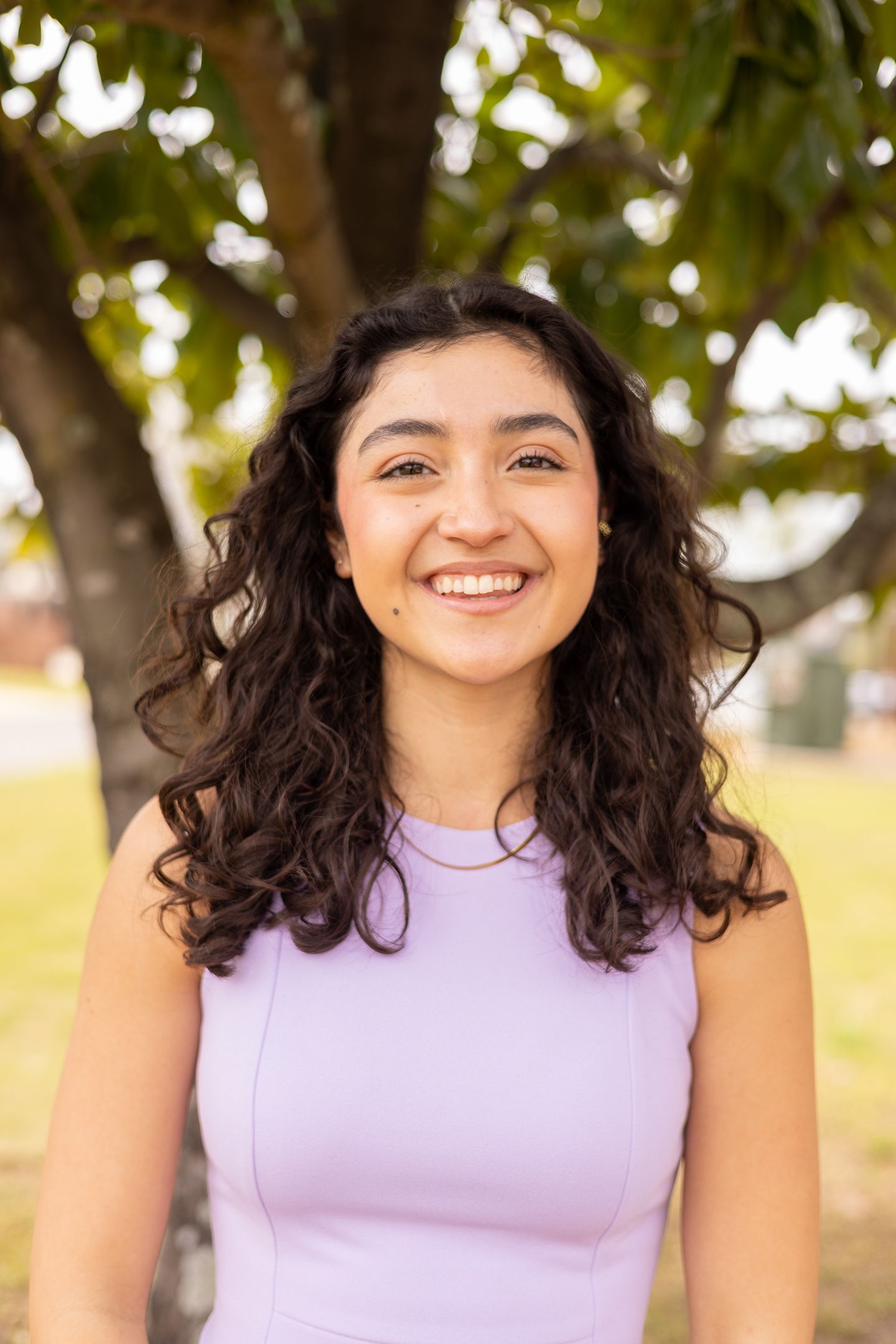 Camila smiles into the camera with a tree behind her