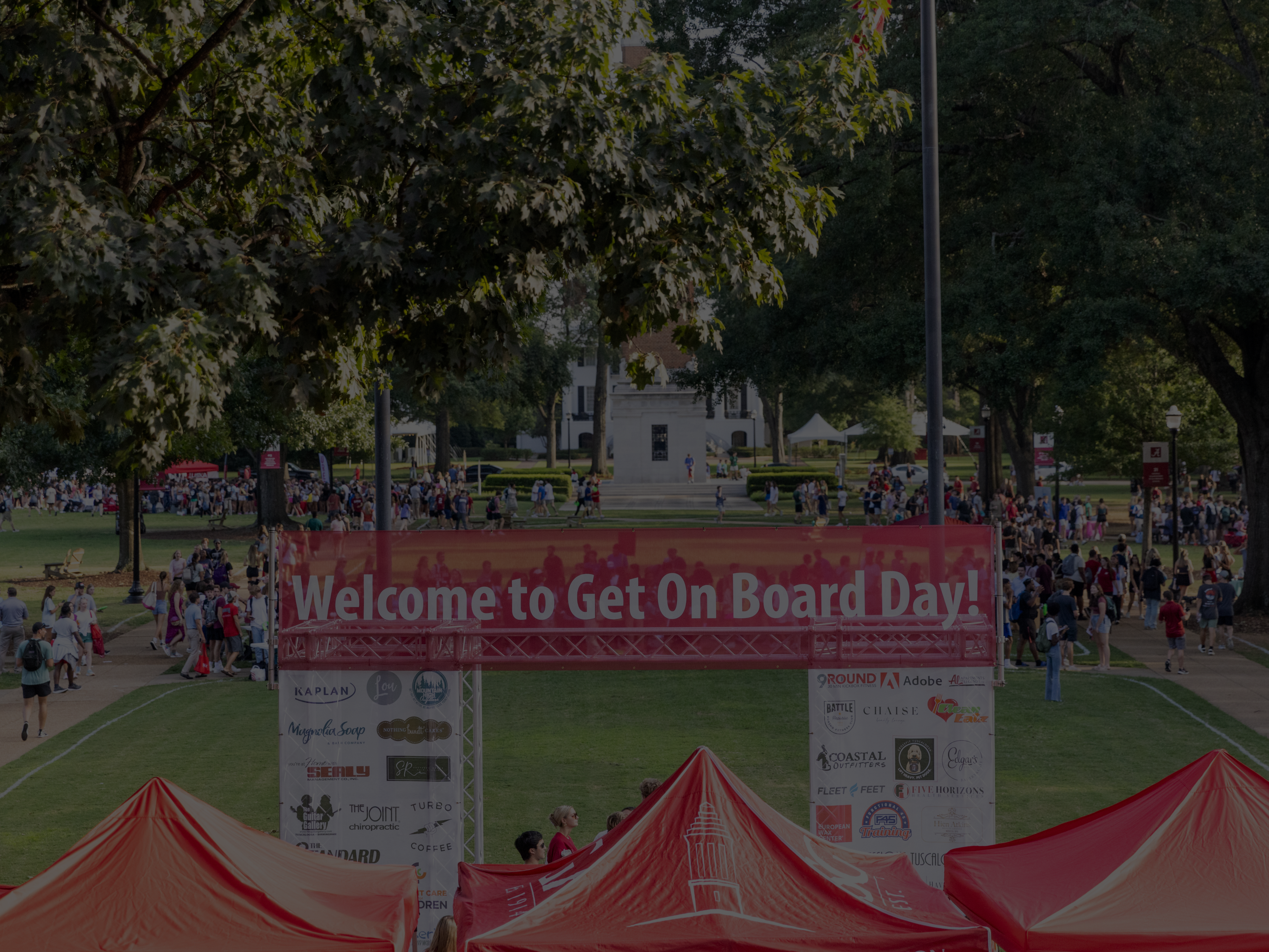 a sign says welcome to get on board day with people walking around it