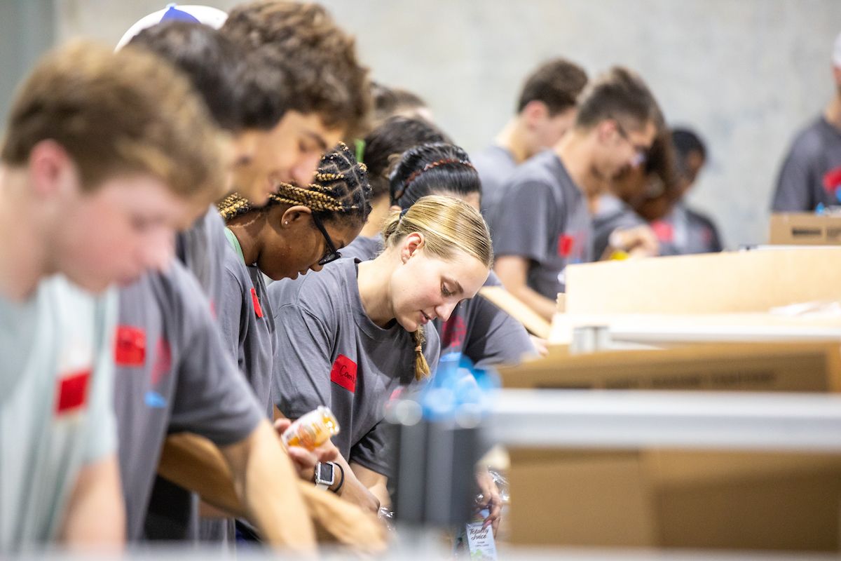 a line of people filling boxes with various goods at a volunteer event