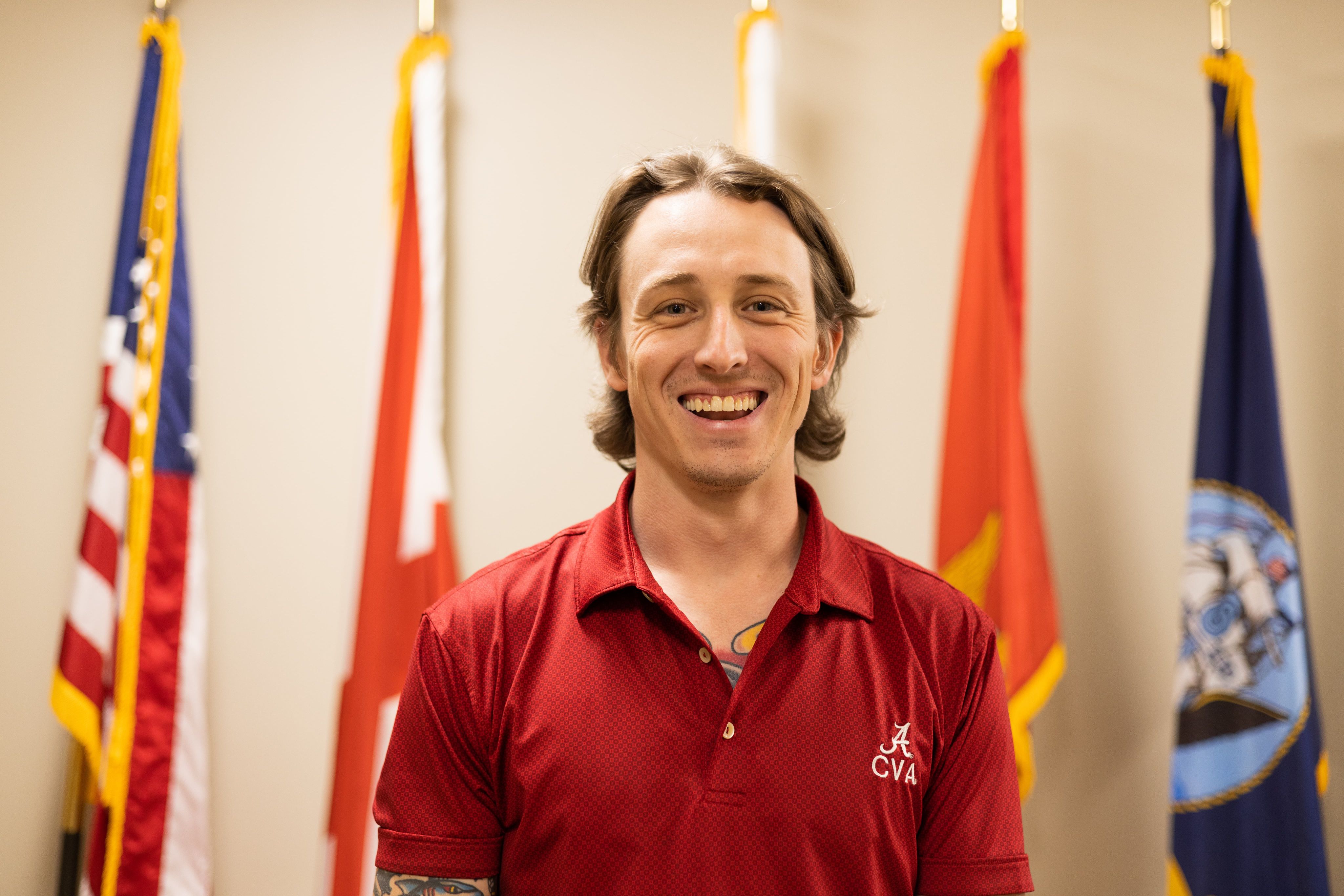 Jordan Golden smiles into the camera with multiple flags behind him