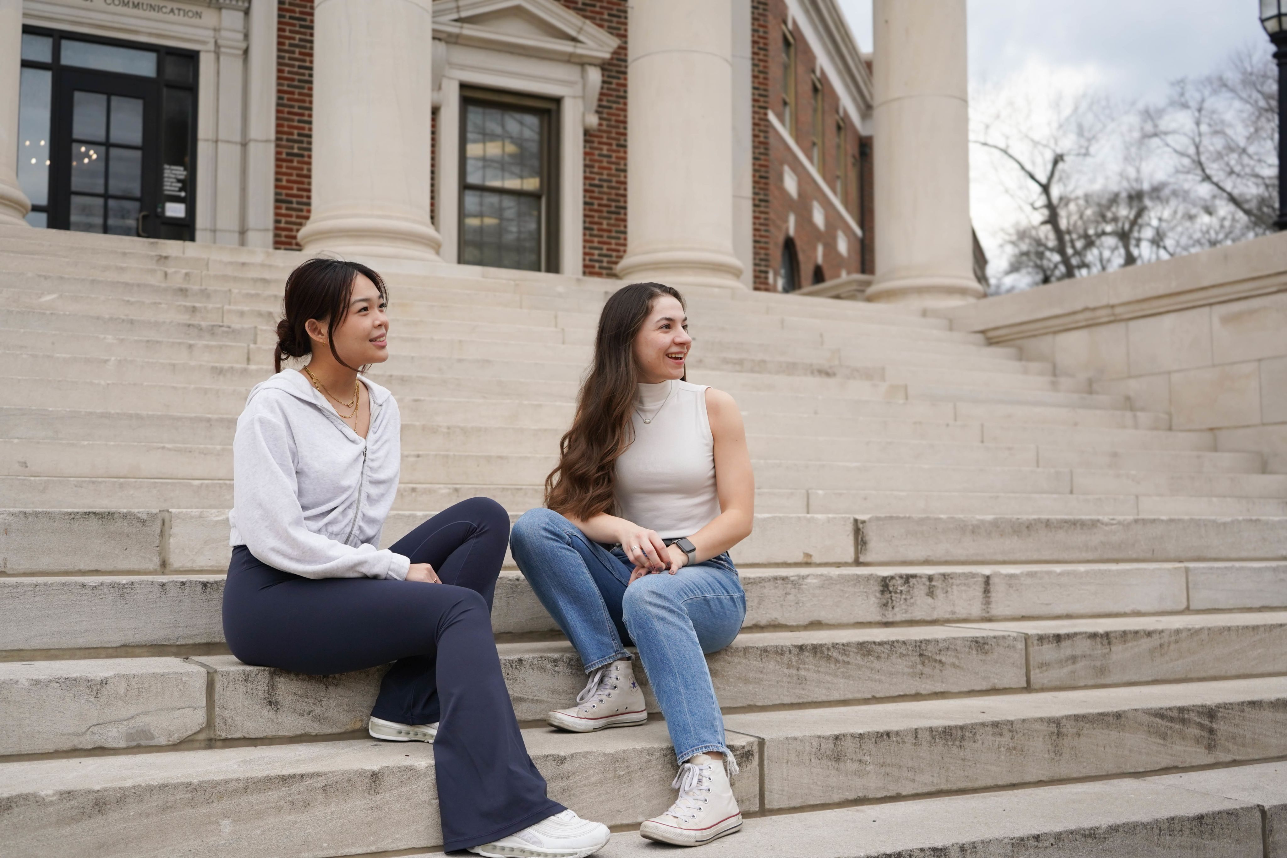 two students sit on steps and talk to another