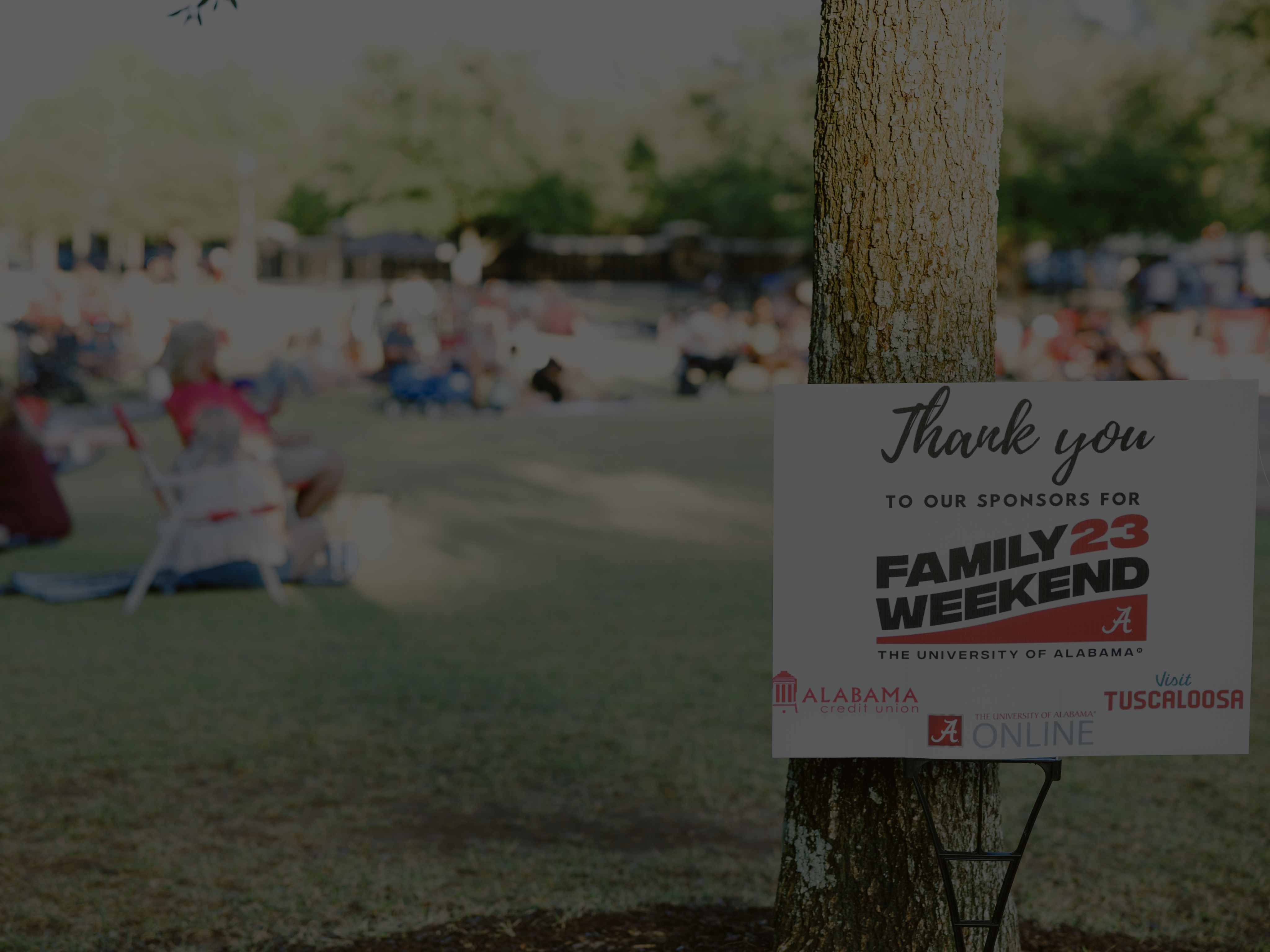 a sign says thank you to our sponsors for family weekend 23 with a crowd of people sitting in the background
