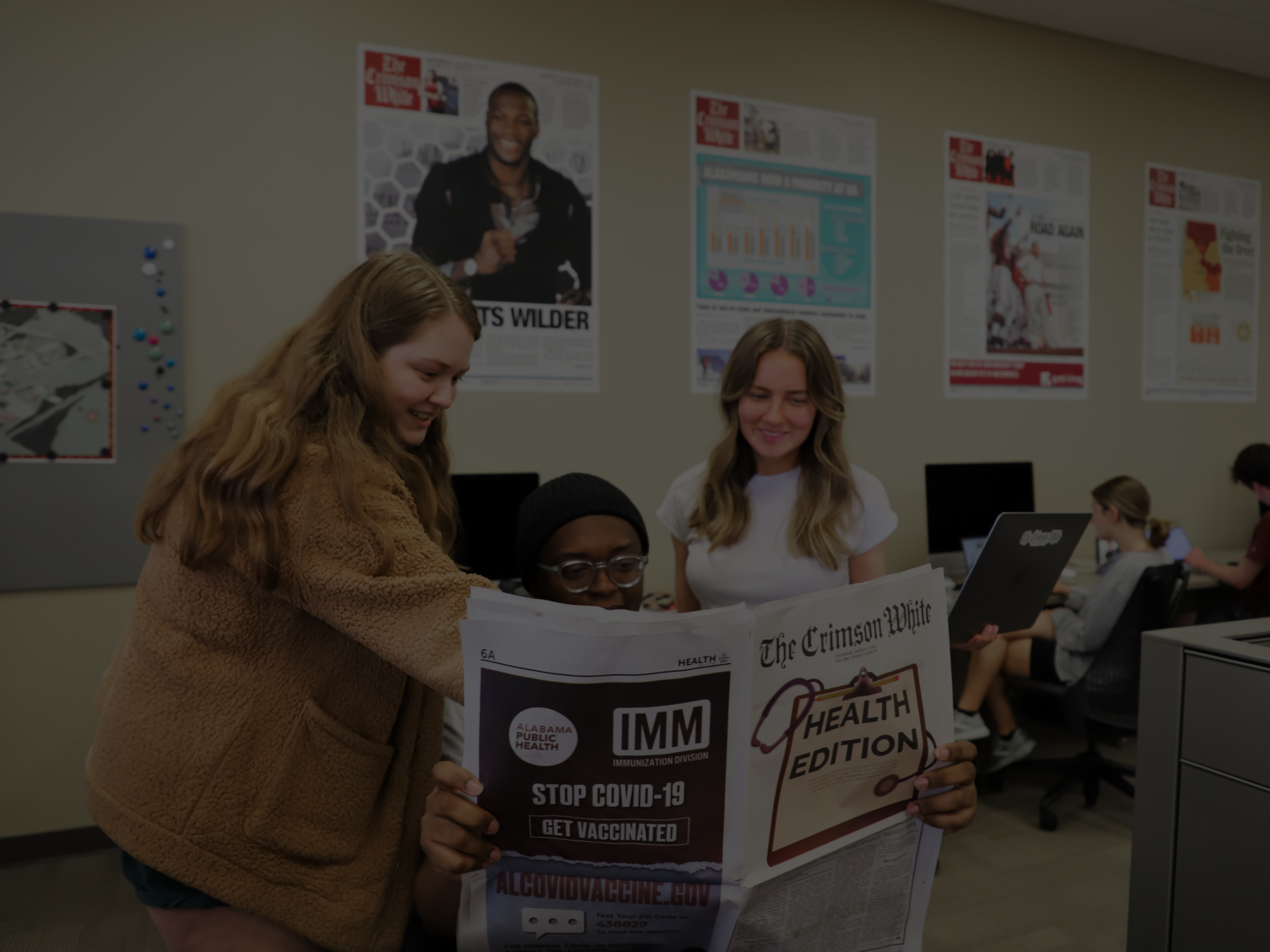 students sit in the newsroom holding a copy of the crimson white newspaper