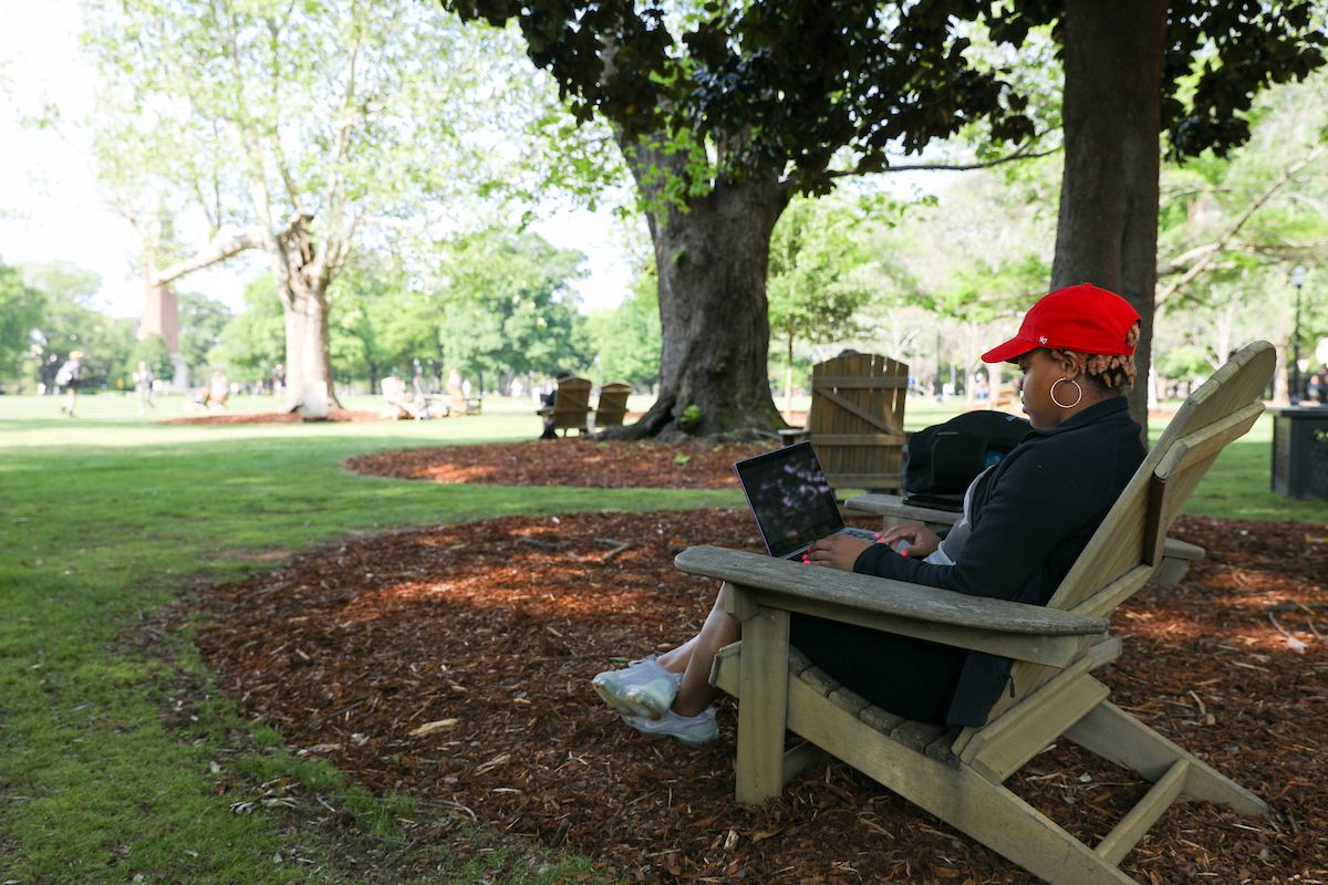 a student sits on a chair on the quad with her laptop