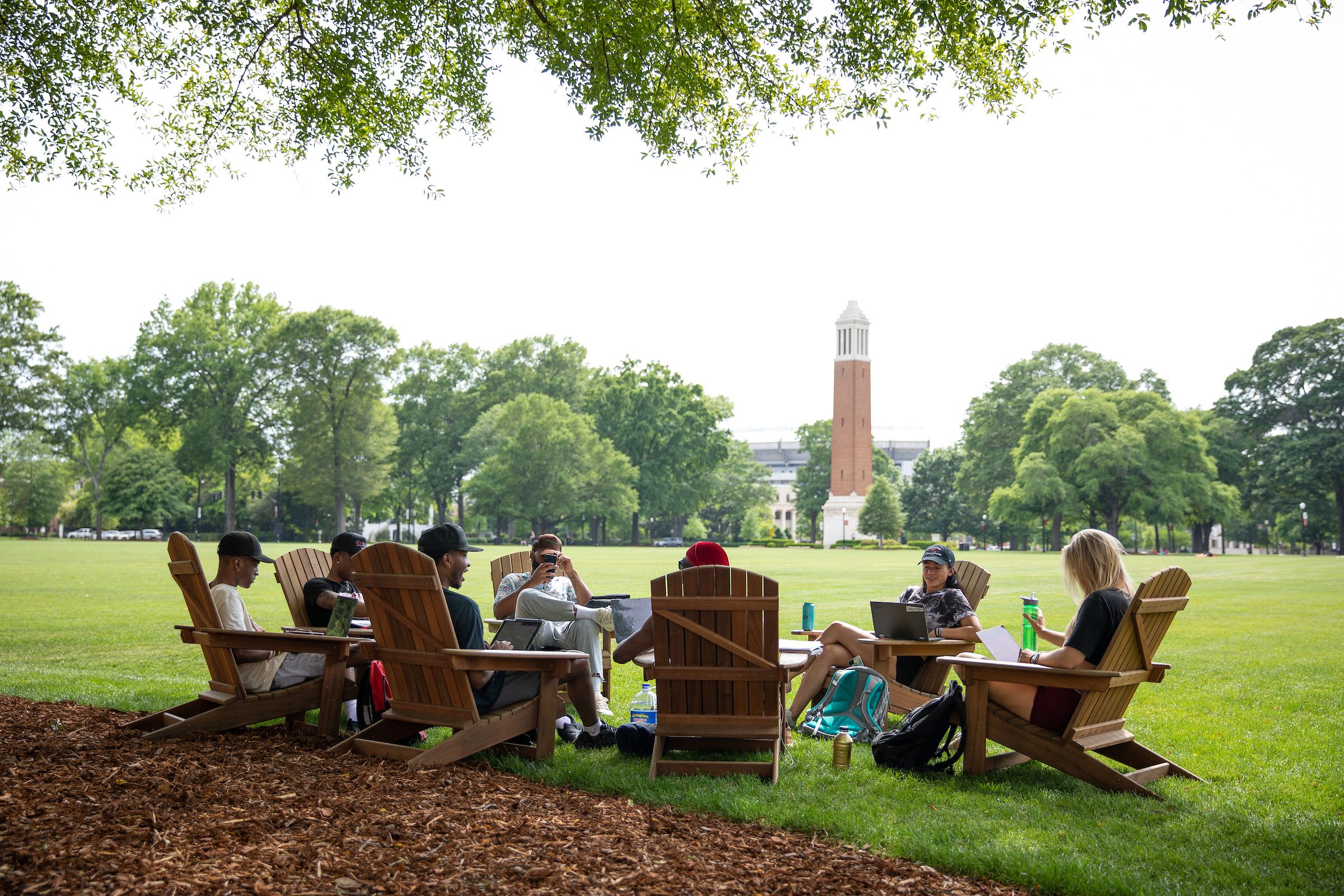UA students relaxing in Adirondack chairs with Denny Chimes in the background