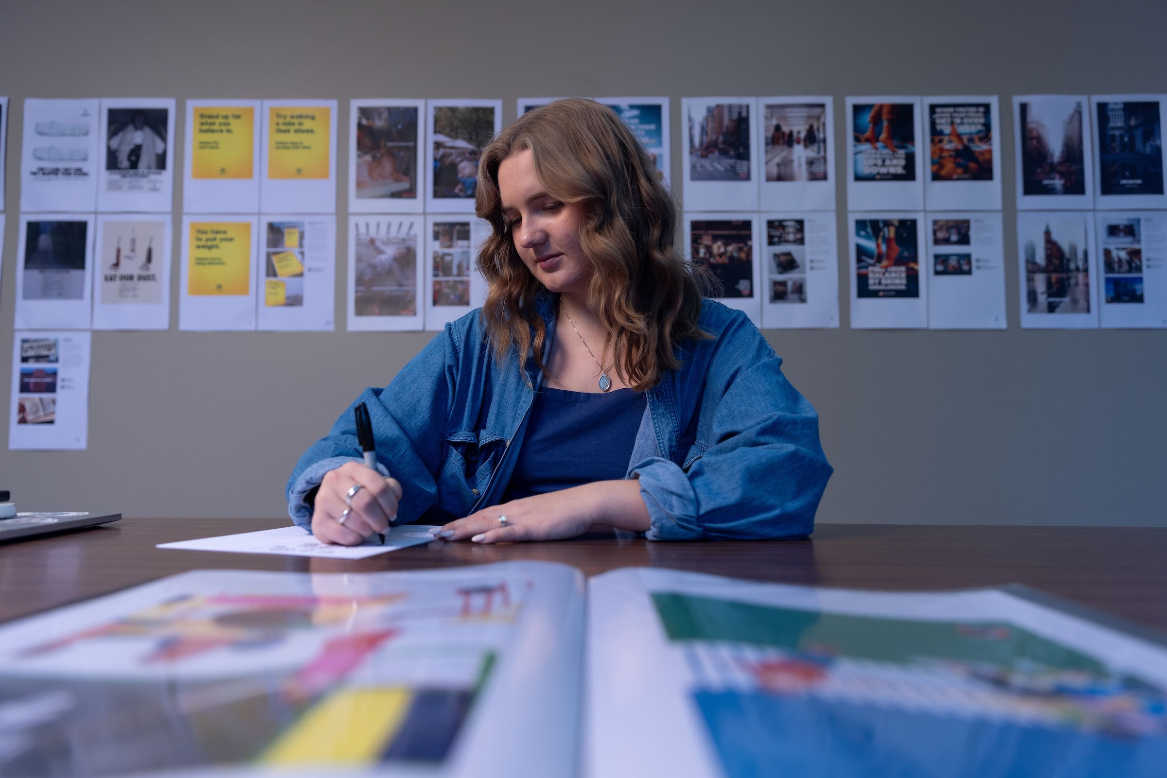 UA student sitting at desk with publications spread on desk in front of them, and on wall behind them.