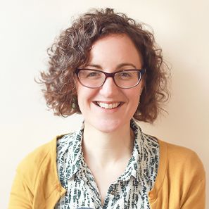 A person with curly hair and glasses, smiling and wearing a patterned shirt.