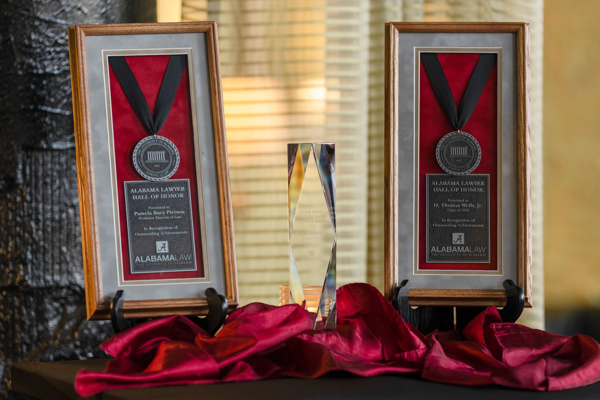 Two framed medals and a glass award on a table with a red satin tablecloth. 