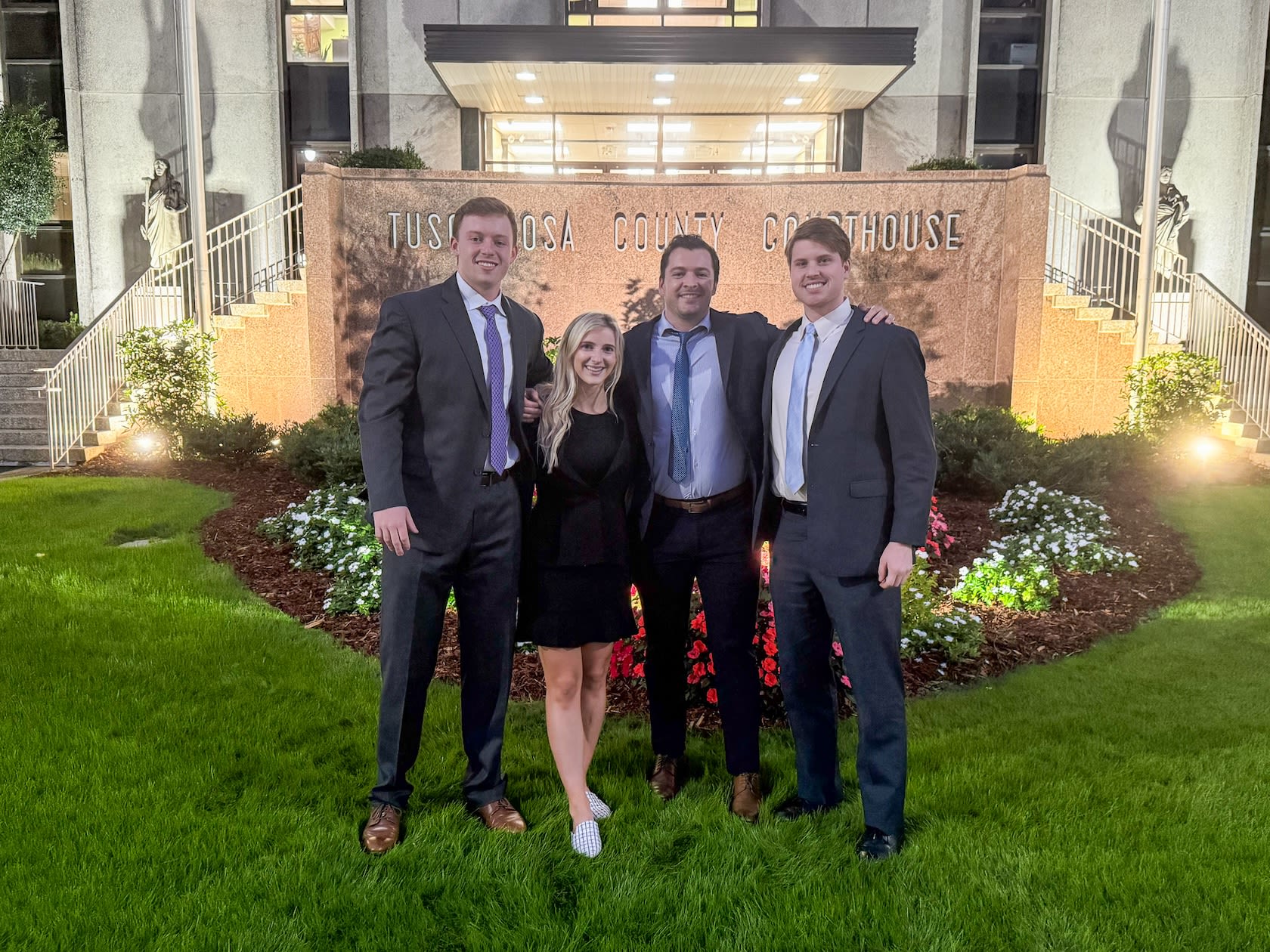 Four law students dressed in business attire stand in front of the Tuscaloosa County Courthouse