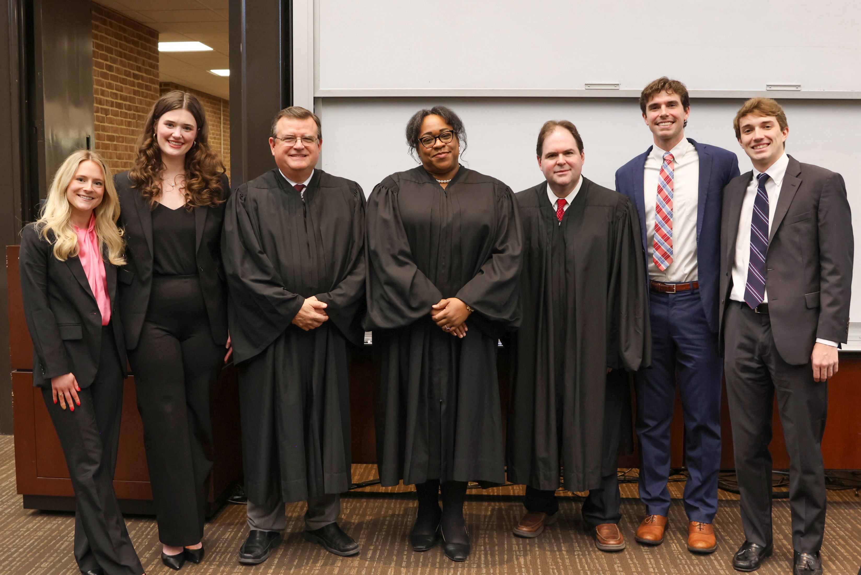 A group of seven people. The three people in the center are dressed in judge's robes. On the left side of the photo is a pair of two women, and two men are on the right. They are all in business attire.