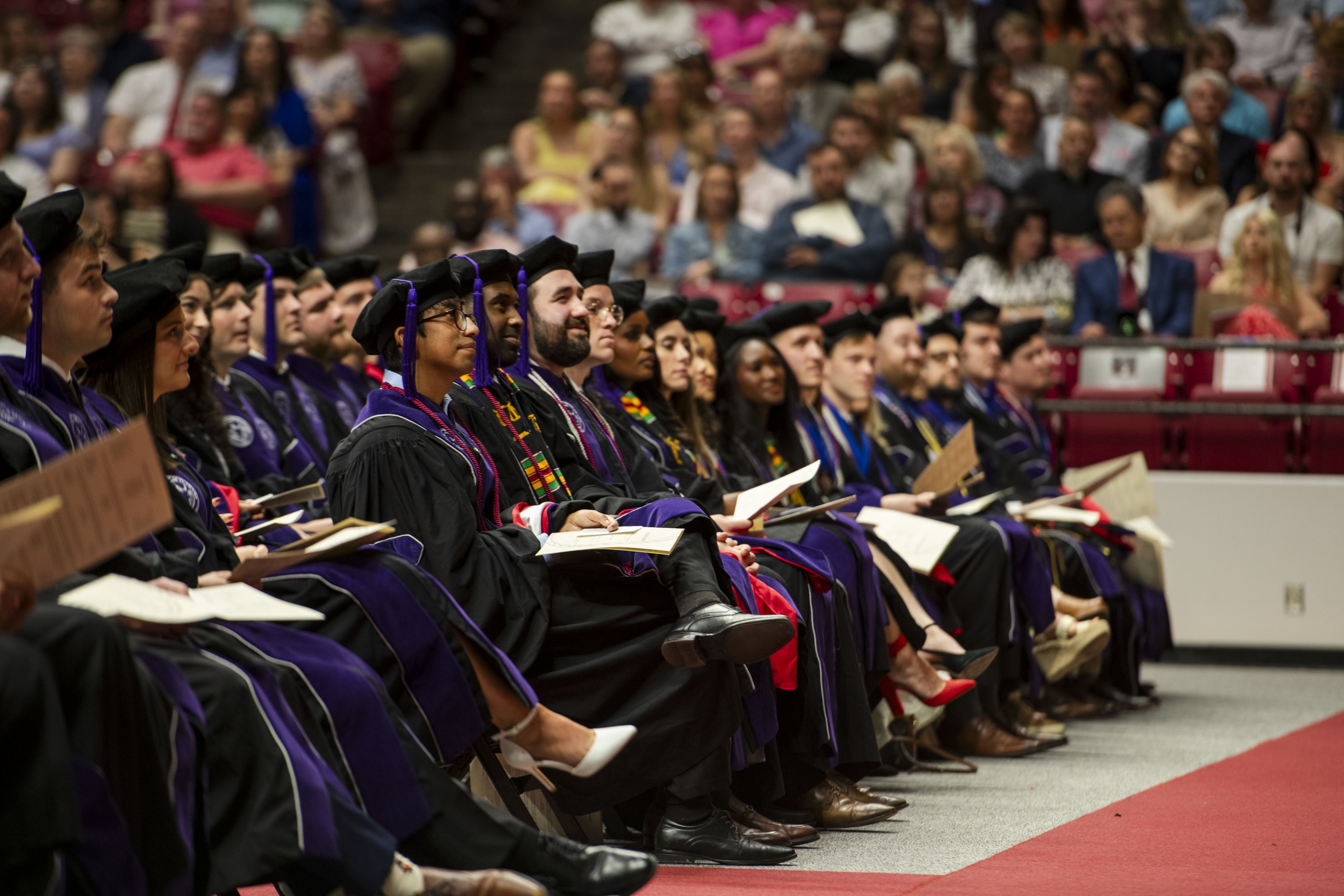 A group of graduates dressed in caps and gowns sitting down.