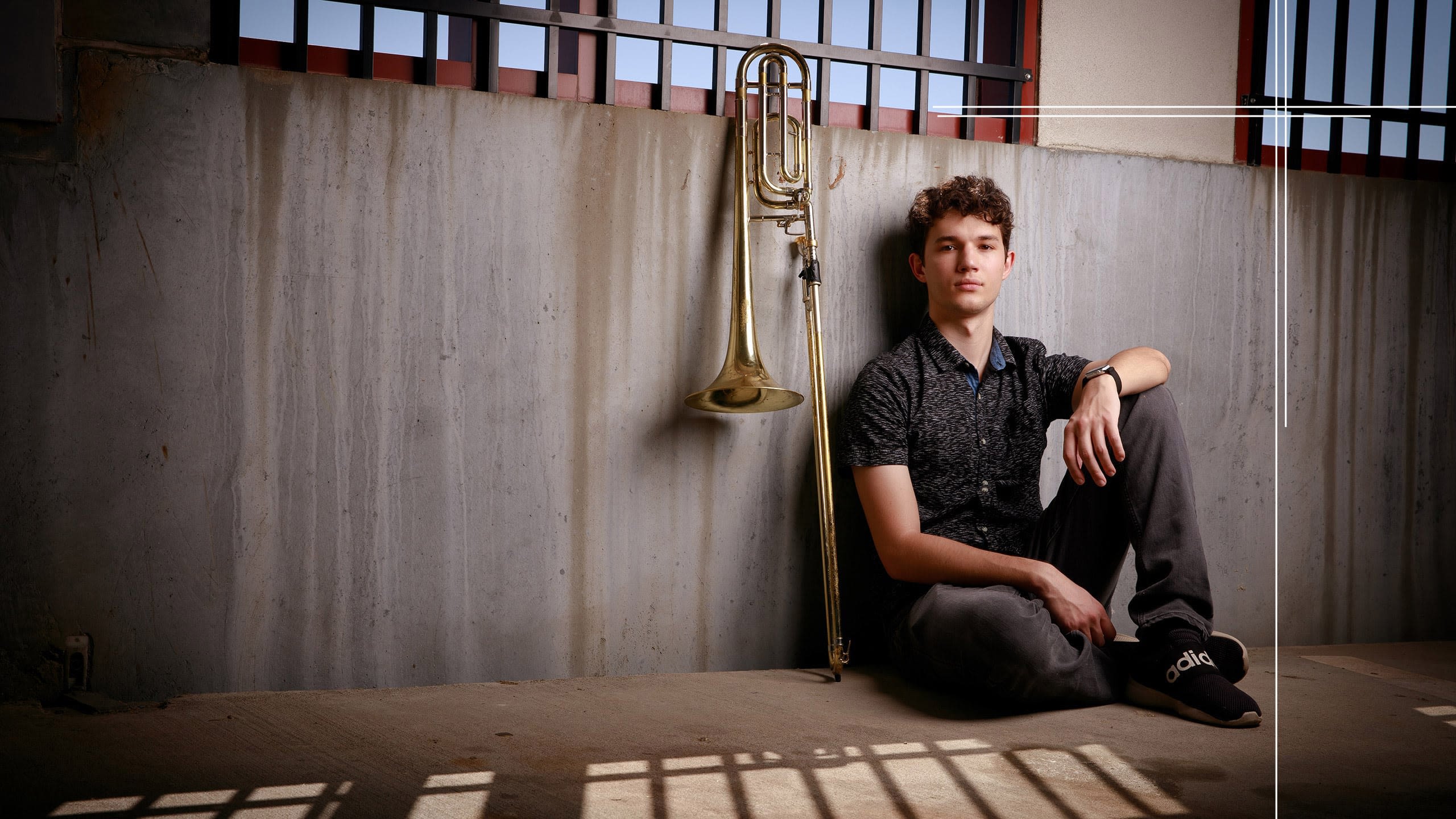 Isaiah sits against a wall with his trombone beside him.