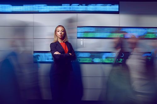 Ellery stands in front of a digital wall displaying stock indices in the College of Business.
