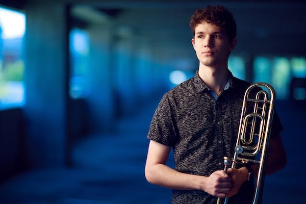 Isaiah stands with his trombone in a concrete structure.
