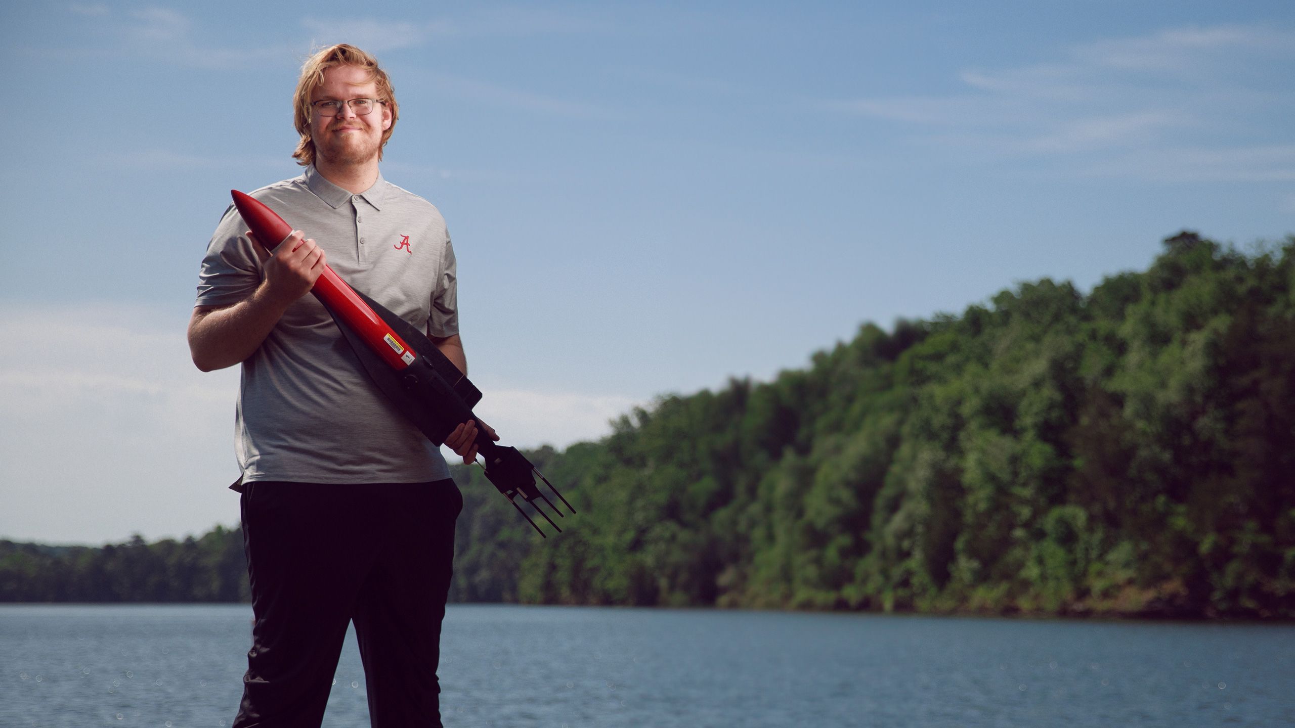 Brodie Alexander standing by a lake holding a piece of equipment.