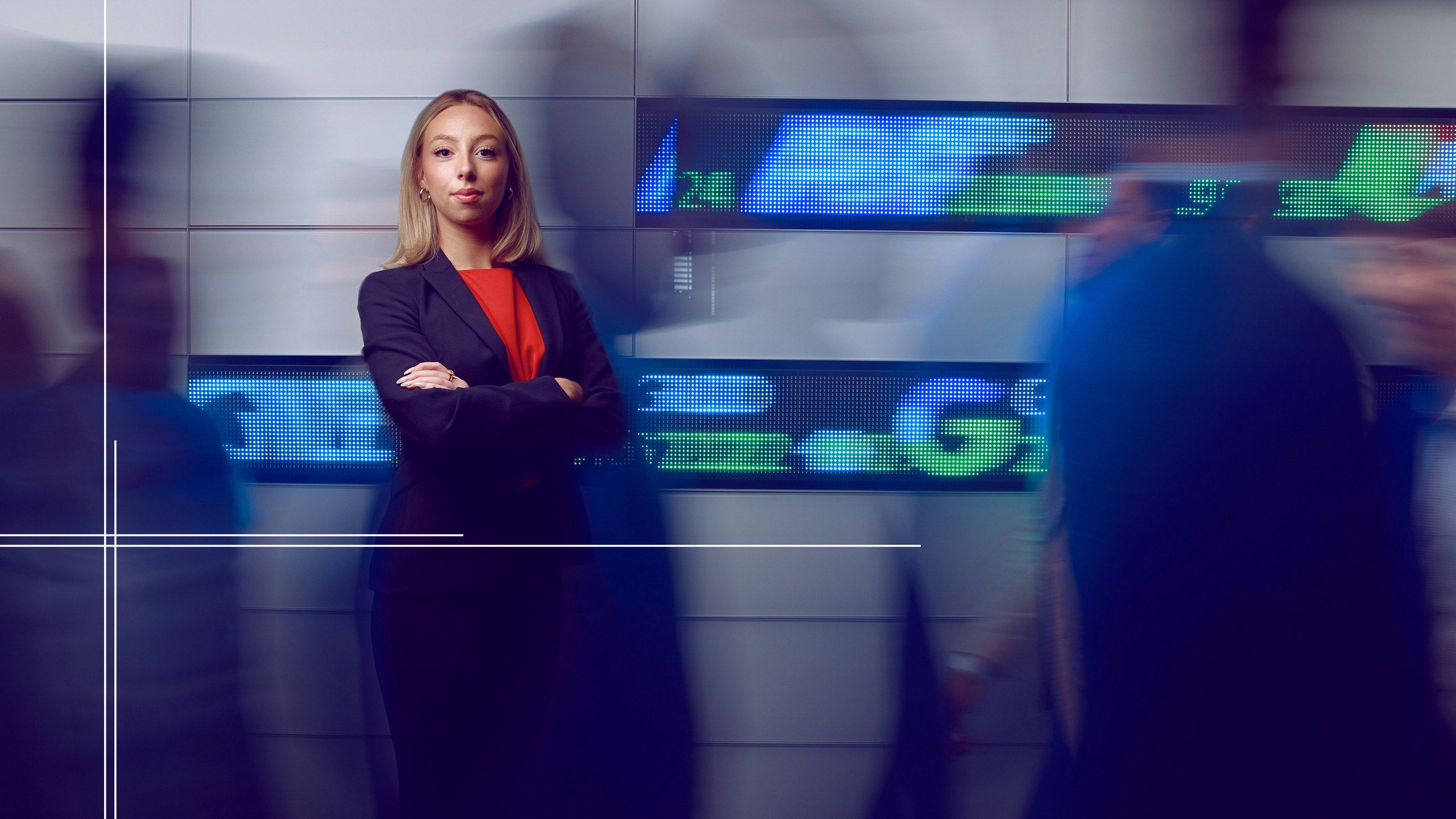 Ellery stands in front of a digital wall displaying stock indices in the College of Business.