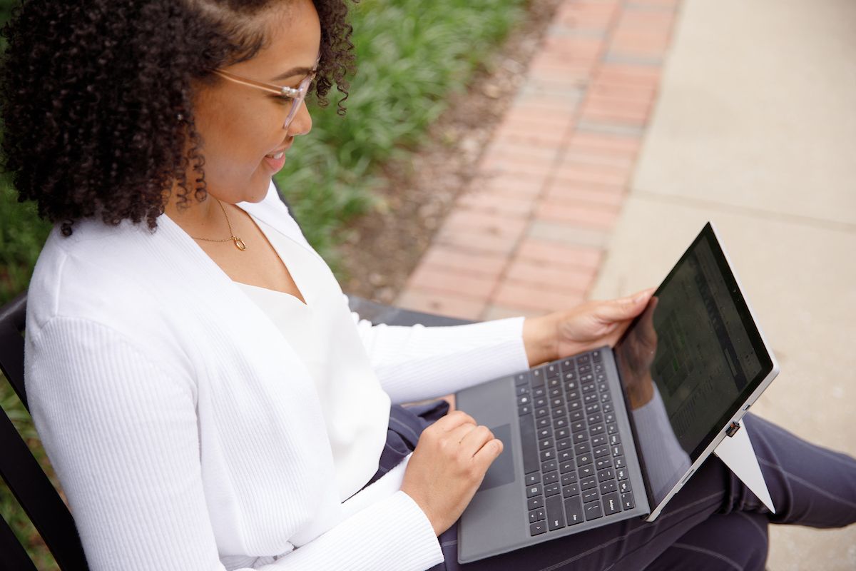 graduate student sitting on park bench holding a laptop