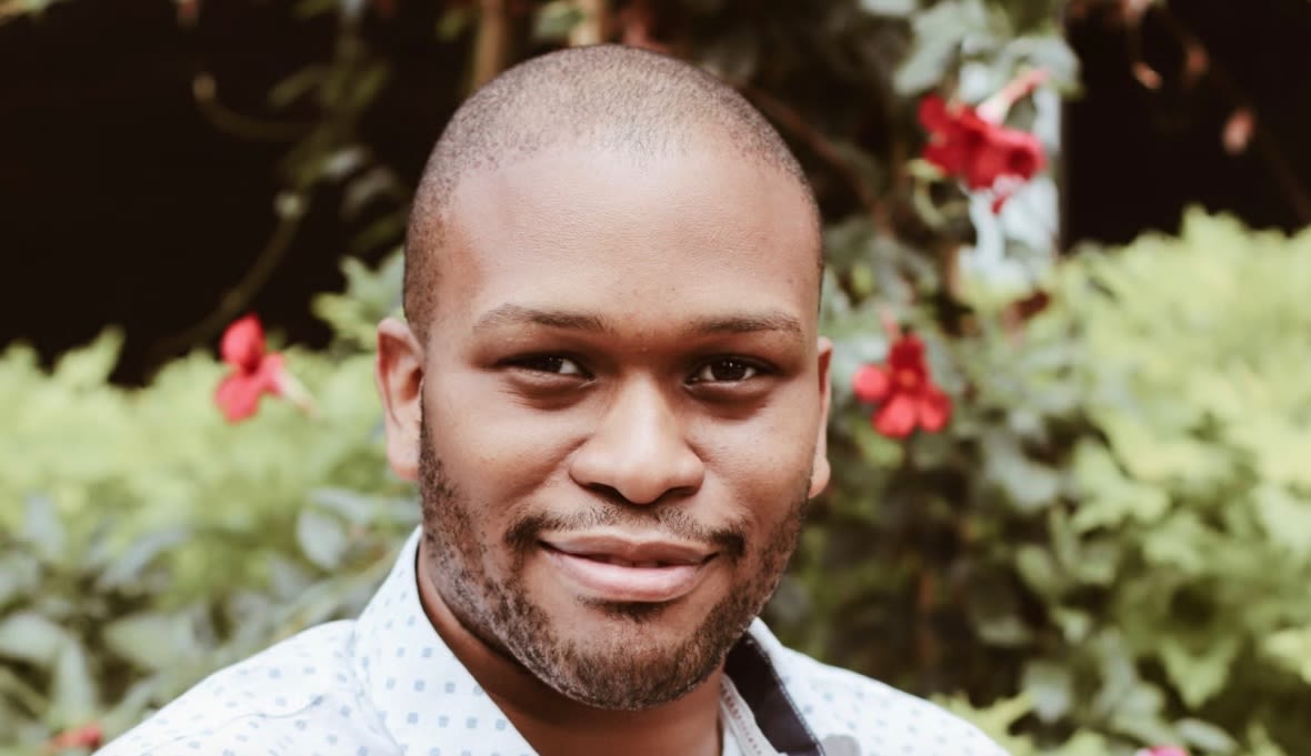 Graduate Student Patrick Talley posing outside near flowering shrubs