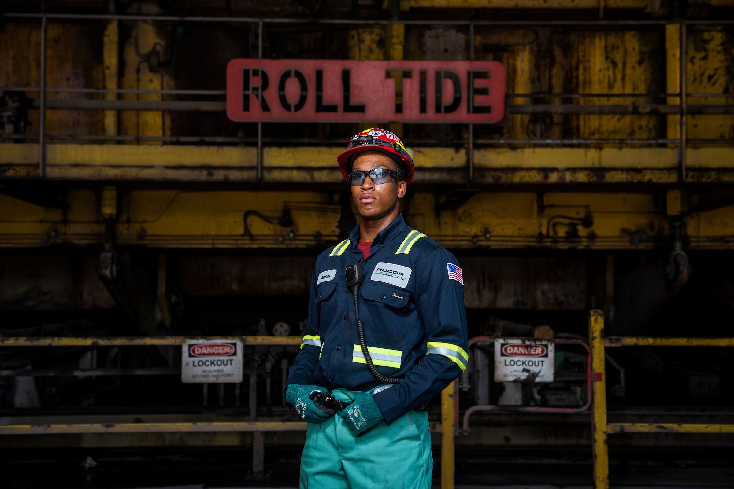 A steel worker stands beneath a metal sign reading ROLL TIDE
