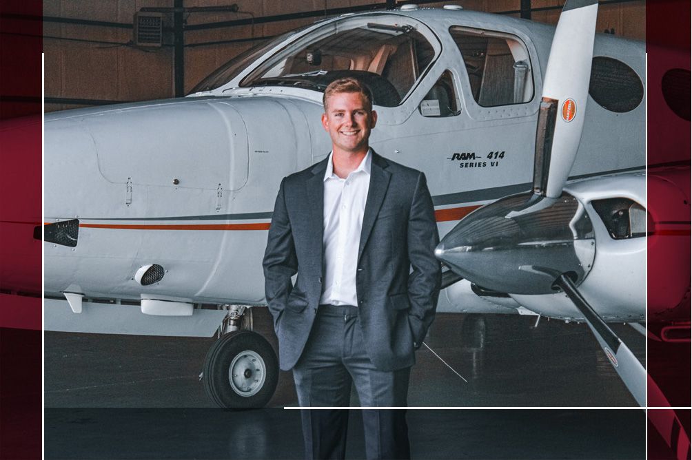 Zac stands in a hangar in front of an airplane.