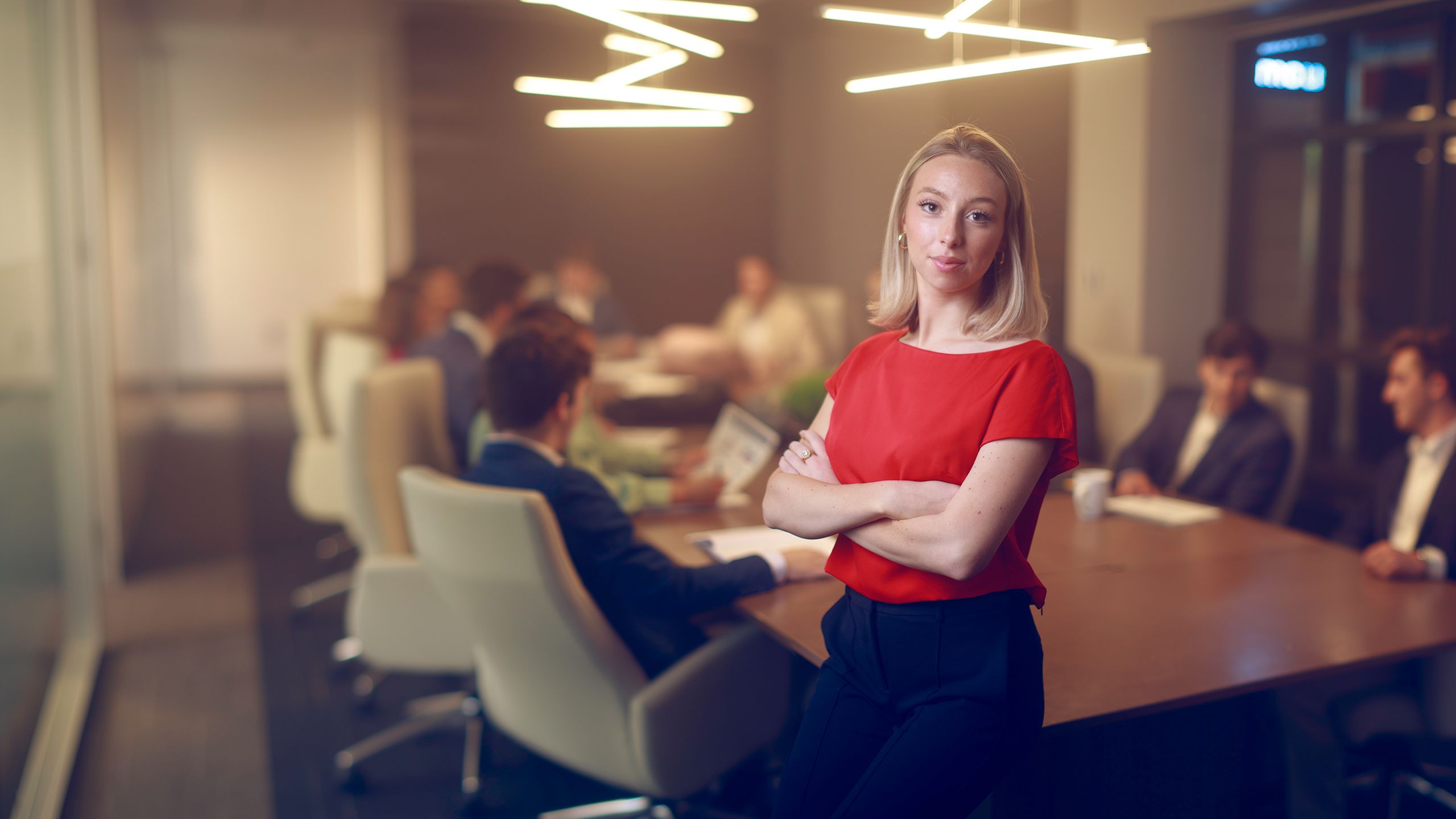 Ellery stands in front of a board room table while a meeting takes place behind her.
