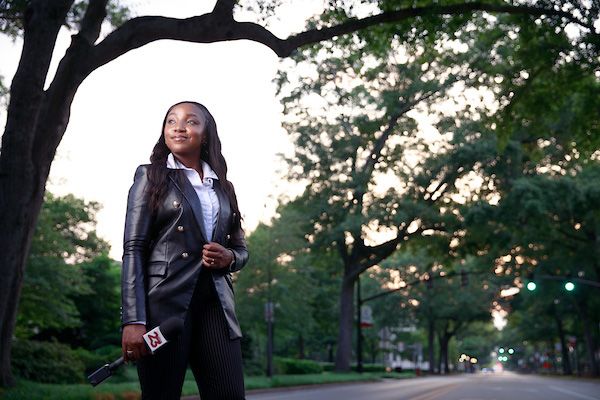 Kennedy stands near a tree on the Walk of Champions holding her microphone and gazing forward.