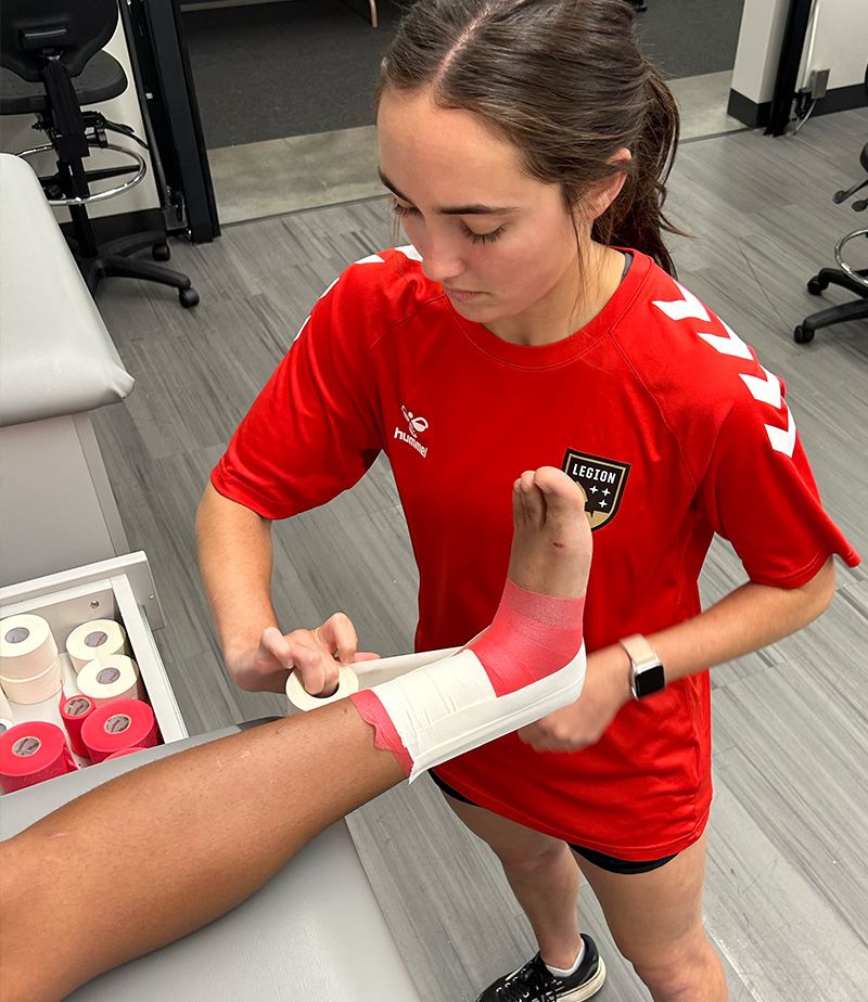 Brittany Grigorian taping up the ankle of an athlete.