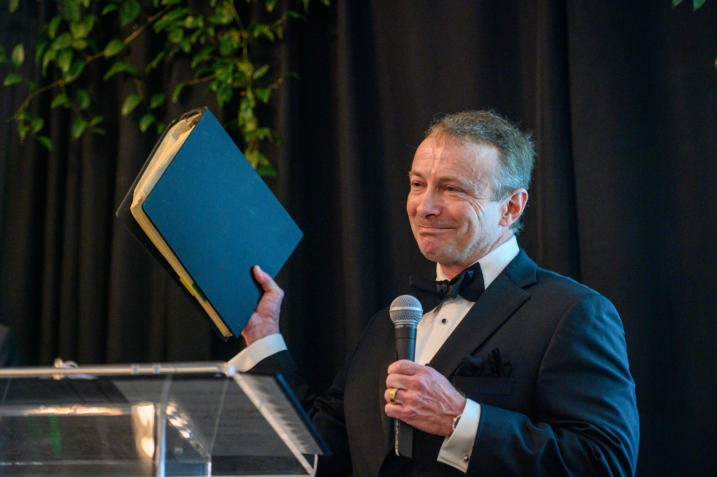 John Baschab giving his awardee speech, holding a binder and a microphone.