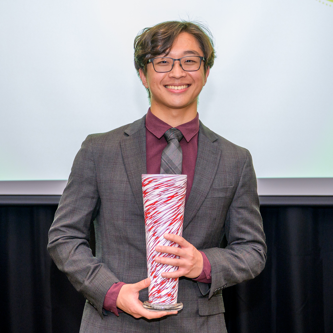 A photo of Jesse Park as he holds his award, a crimson and white vase.