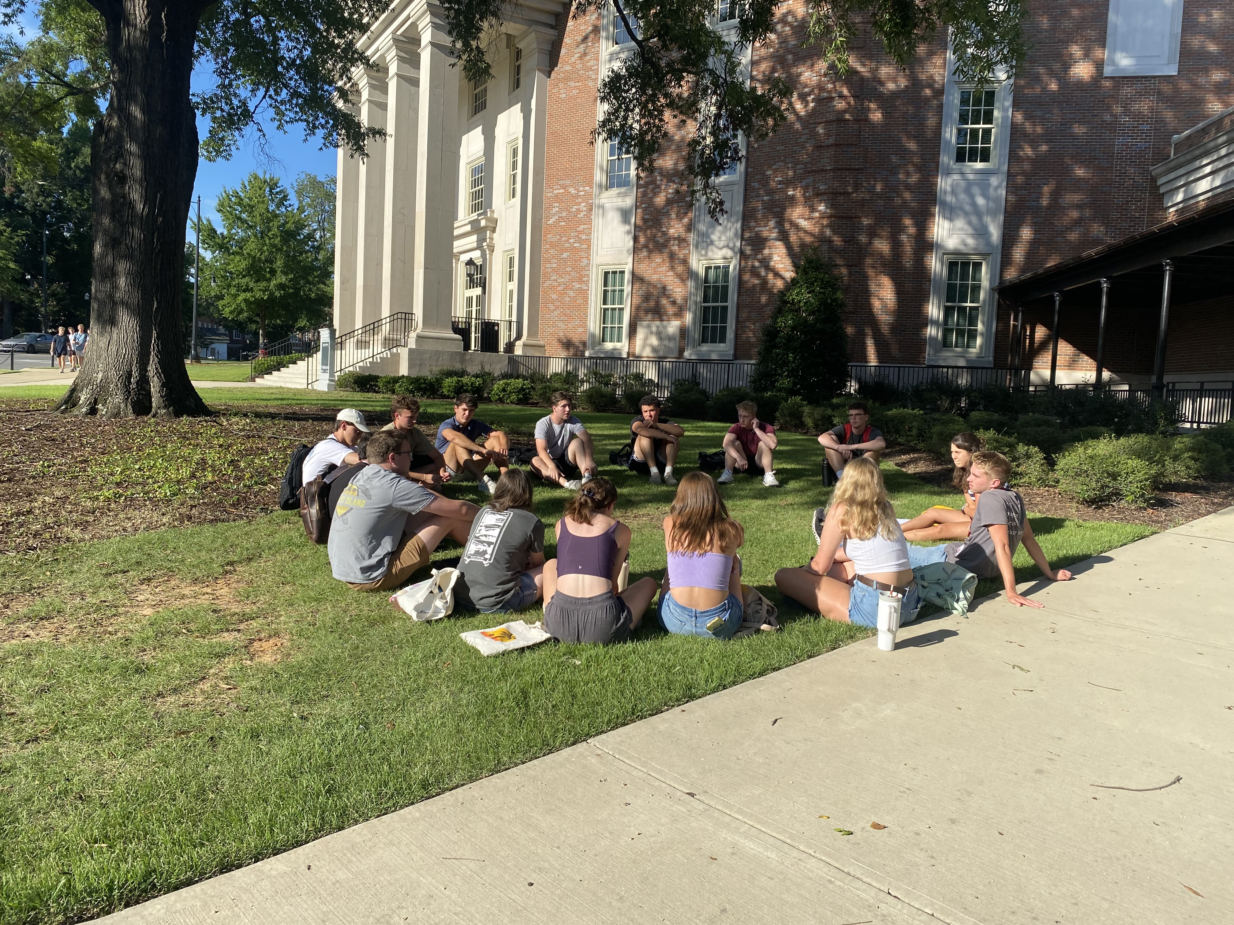 A group of Honors students sit in a circle outside on the grass.