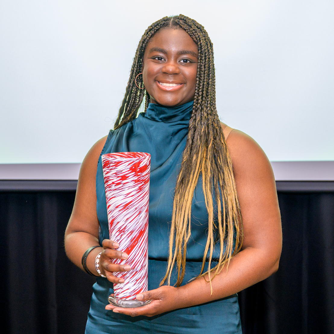 A headshot of Phanuelle Manuel, she holds her Honors College award, a crimson and white vase.