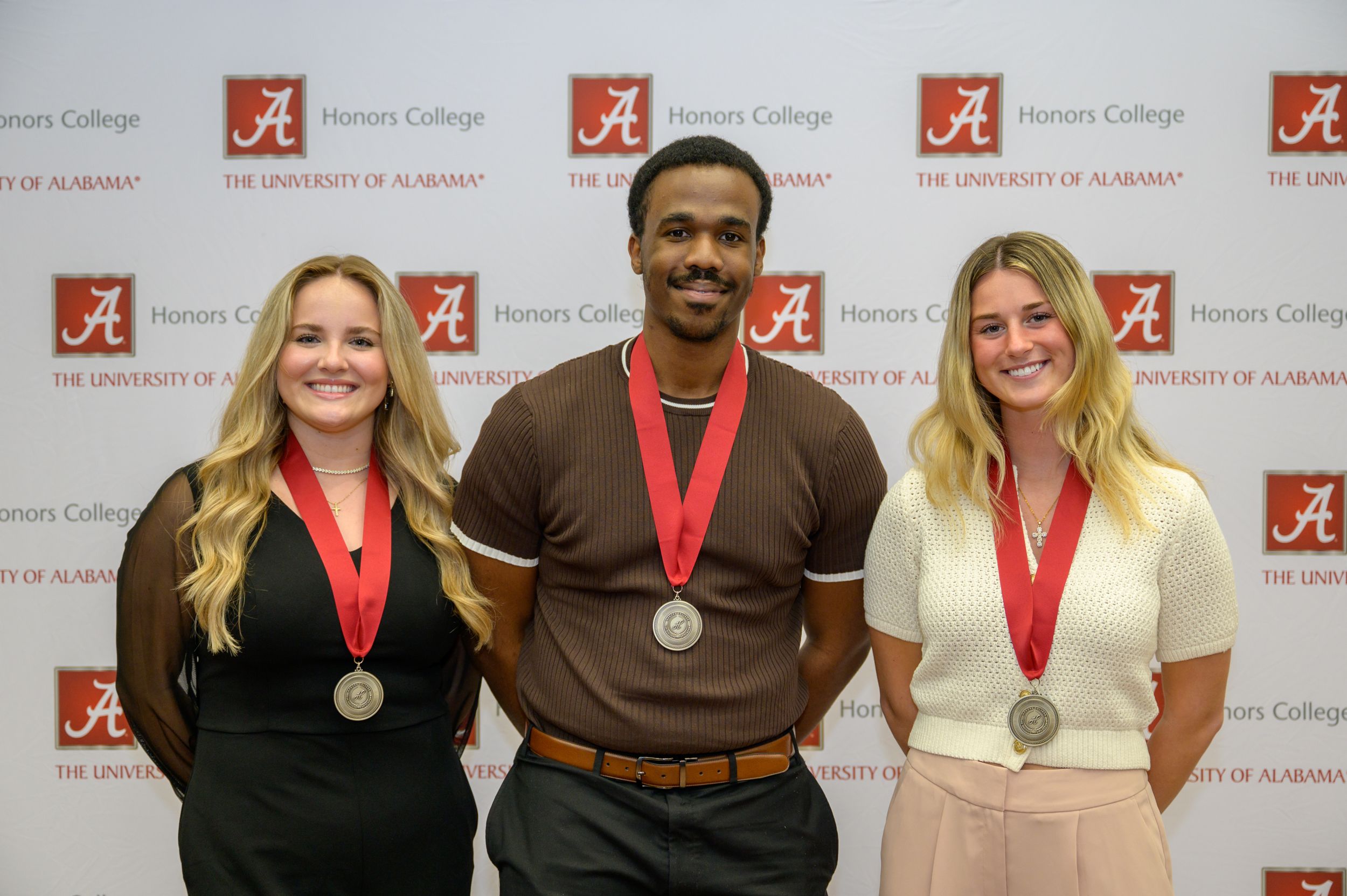 Three Honors College graduating seniors smile while wearing their Honors medallions.